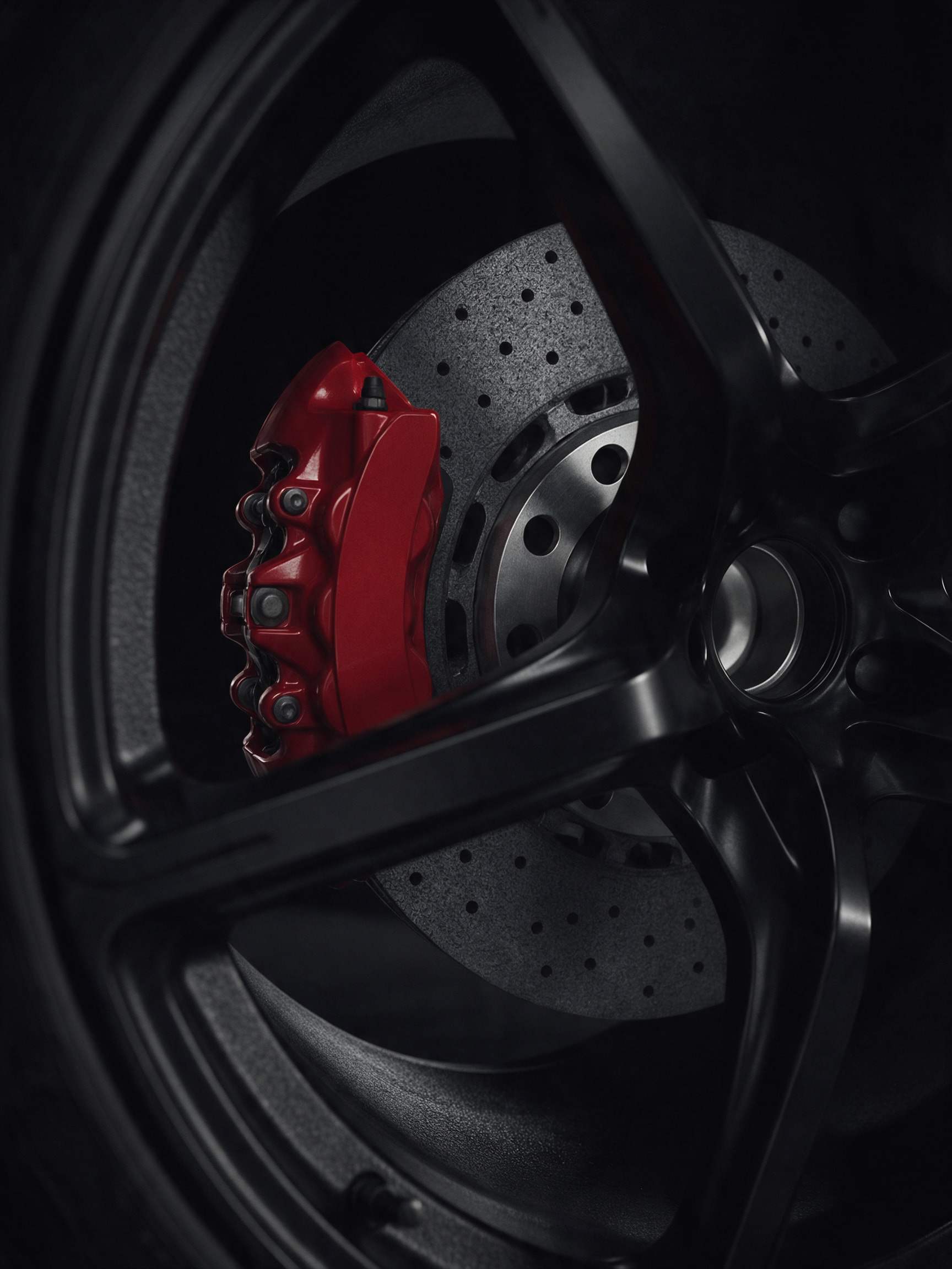 Red six-piston brake caliper behind a drilled carbon-ceramic disc